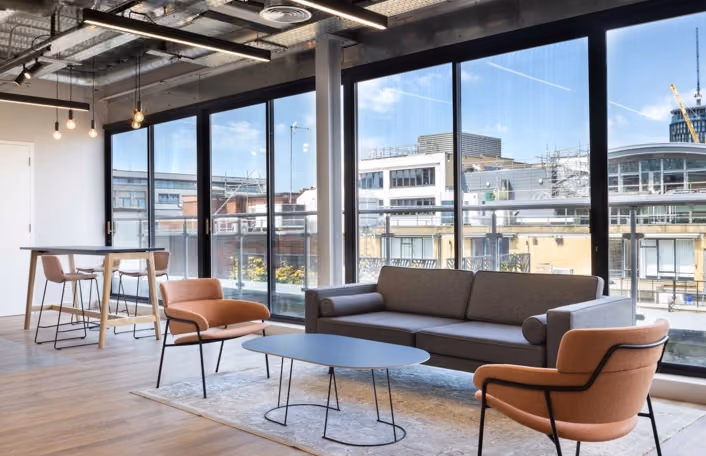 Breakout area with a sofa, two armchairs, and a coffee table, featuring large windows with an outdoor view.